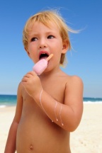 American child enjoying eating ice cream bar at the beach.  The child is normal weight for a 3 year old, however her waist is larger than her hips.